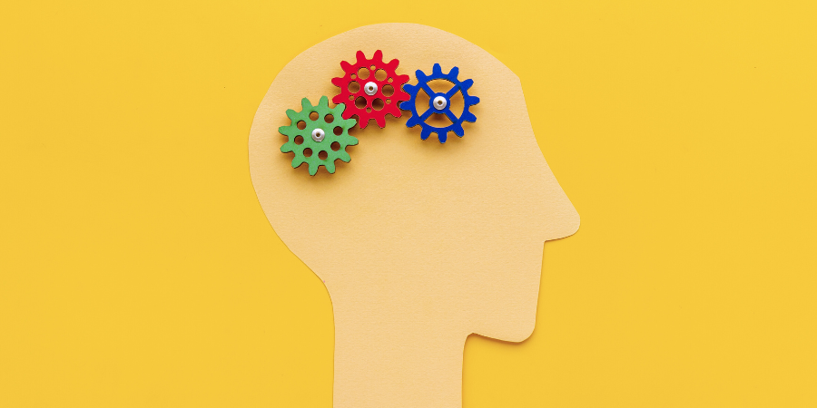A yellow background with a paper cutout of a human head with gears turning over the brain area.