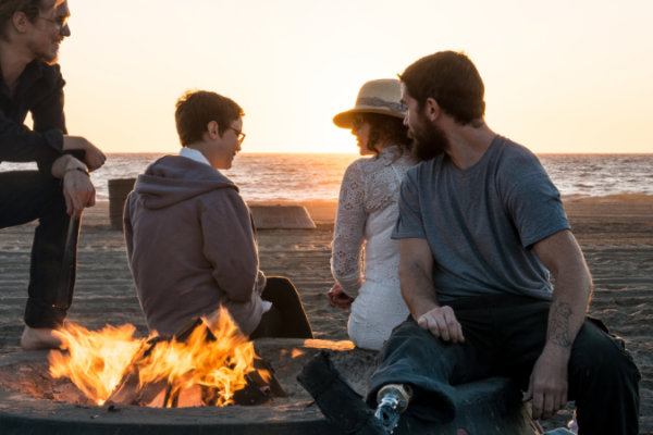 Four people sitting next to a fire pit on the beach